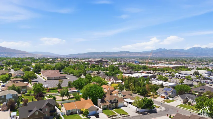 Aerial perspective showcasing a residential area with varied home styles, mature trees, and mountainous terrain in the background