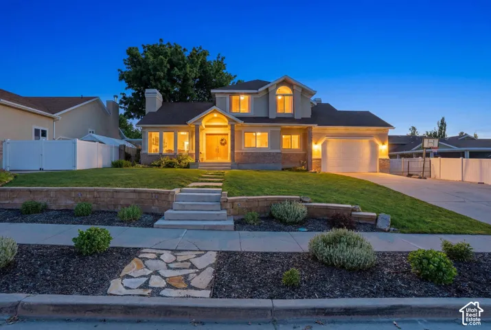 Two-story residence featuring a two-car garage, stone and stucco exterior, arched window dormer, and a tiered front yard with retaining walls and stone path