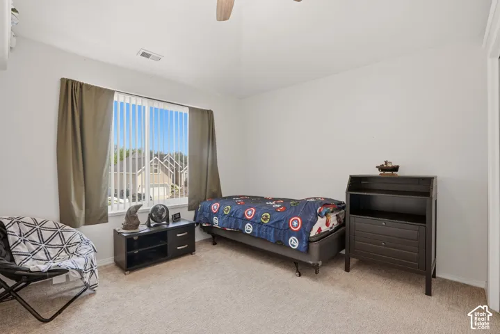 Carpeted room featuring a ceiling fan, a window with vertical blinds and drapes, and a built-in closet