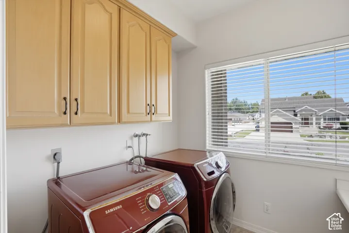 Laundry area featuring upper cabinetry with black hardware, a large window with horizontal blinds, and light-toned flooring