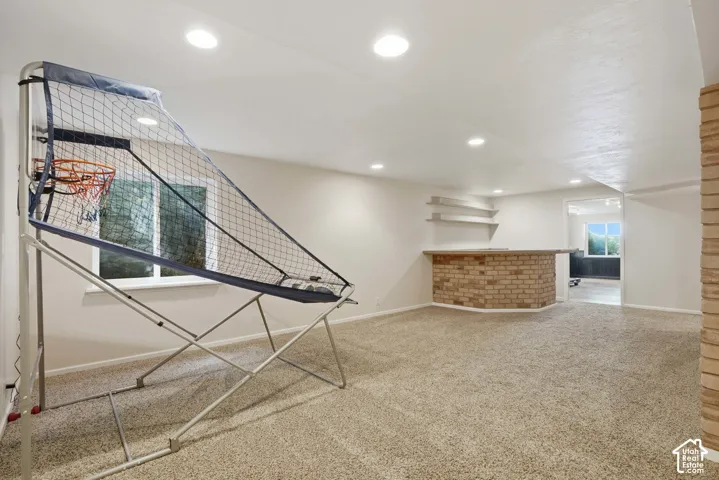 Spacious room featuring neutral carpeting, recessed lighting, a brick-front bar with a wood countertop, and built-in shelving