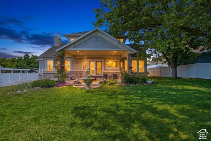 Rear exterior featuring a covered patio, a multi-tiered fountain, a stone and siding facade, a manicured lawn, and a mature tree