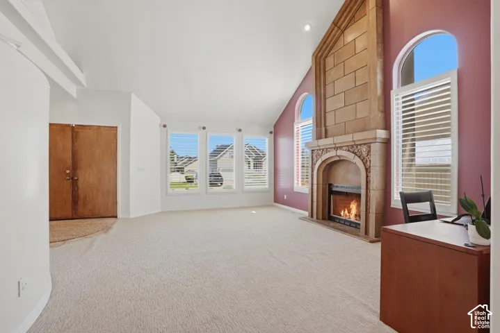 High vaulted ceiling living area featuring a prominent stone fireplace with carved detailing, multiple windows with plantation shutters, and a double-door entry
