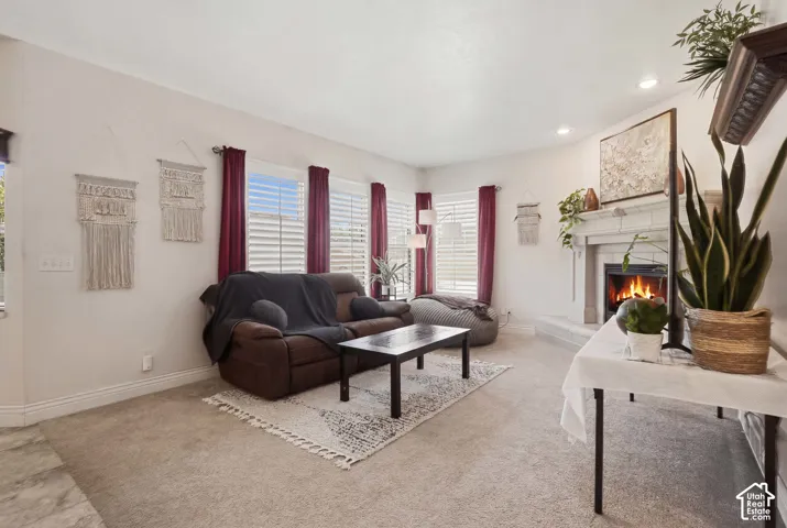 Living area featuring a fireplace with a light-colored mantel, recessed lighting, carpet flooring, and multiple windows with horizontal blinds