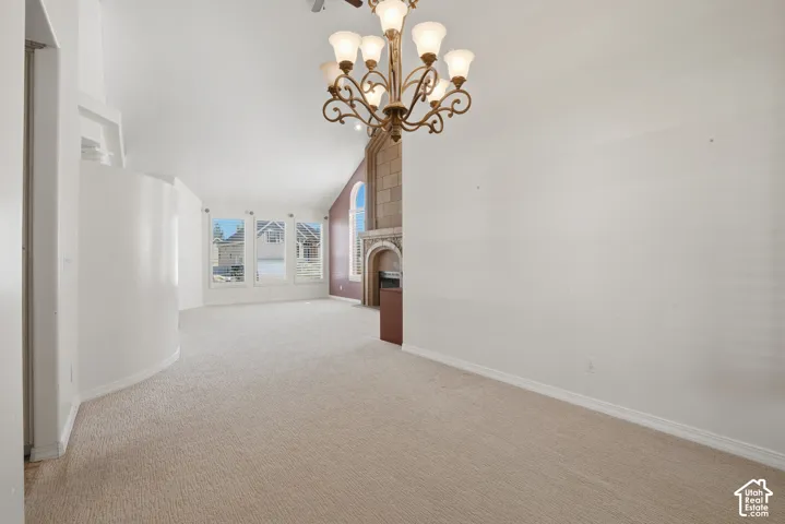 Spacious living area featuring neutral carpeting, a decorative chandelier, multiple windows for natural light, a fireplace with a stone surround, and a curved wall detail
