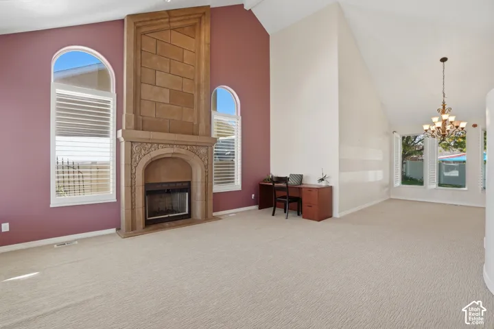Vaulted ceiling living space featuring a floor-to-ceiling stone-clad fireplace with intricate carvings, arched windows with plantation shutters, and light-tone carpeting