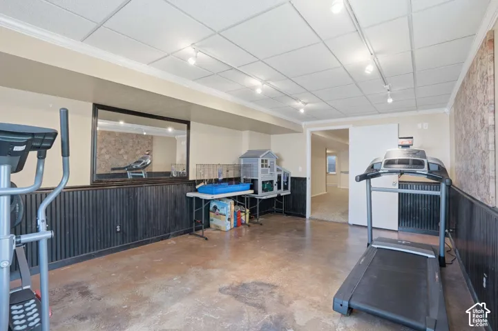 Lower level space featuring stained concrete flooring, dark wood paneling, a drop ceiling with track lighting, and a mirrored wall accent