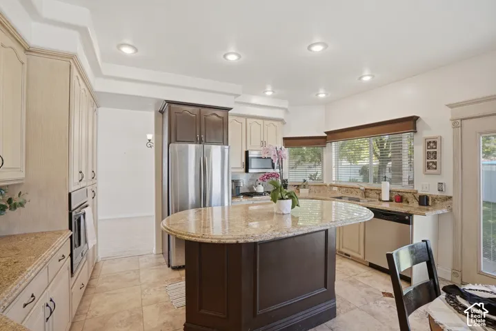 Contemporary kitchen featuring an elliptical island with a granite countertop, recessed lighting, tile flooring, stainless steel appliances, and a double window with blinds