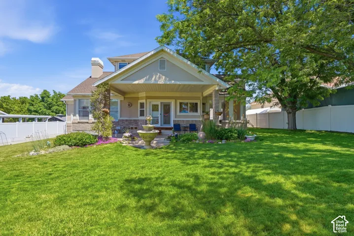 Front exterior featuring a covered porch, stone facade accents, an architectural chimney, a manicured lawn, and a mature shade tree