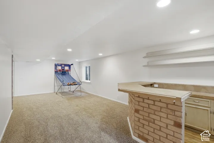 Finished basement featuring recessed lighting, light-toned carpet flooring, a built-in brick-front bar with a light-toned countertop, integrated cabinetry, and open shelving