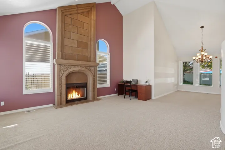 Spacious interior featuring a stone fireplace with ornate carving, arched windows with plantation shutters, vaulted ceilings, and light-toned carpeting