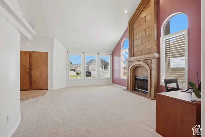 Spacious living area featuring a stone-clad fireplace with intricate carvings, arched transom windows with plantation shutters, vaulted ceilings, and light-toned carpeting