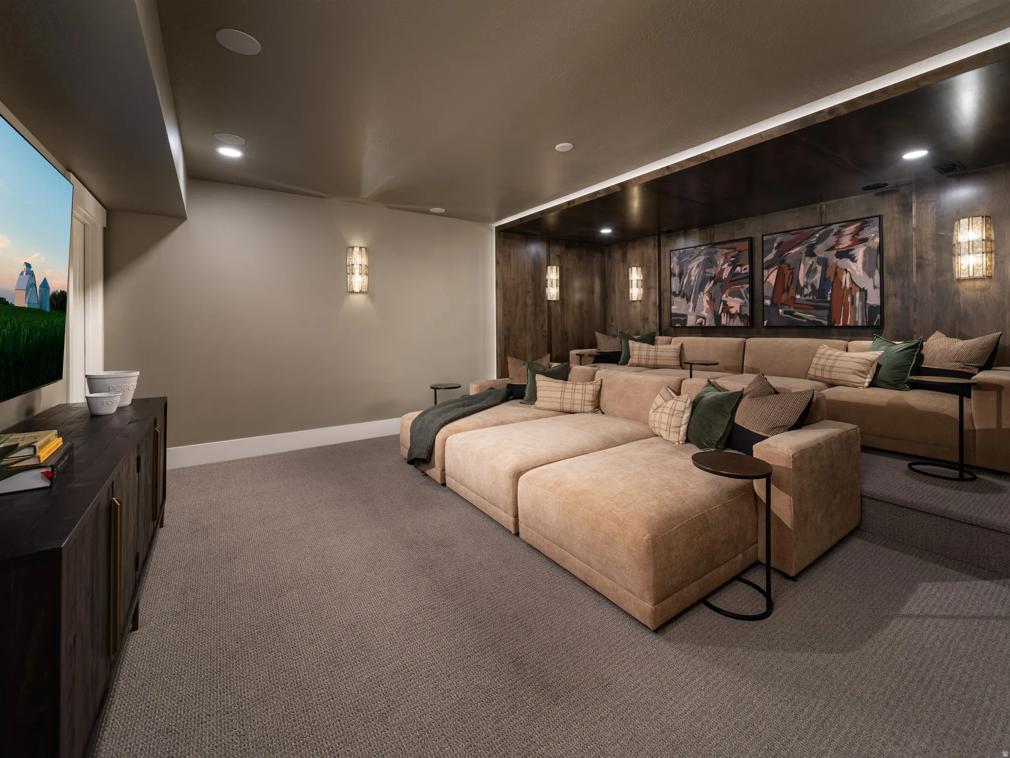 Dedicated media room featuring tiered seating, recessed ceiling lighting, wall sconces, wood paneling, and a built-in media console