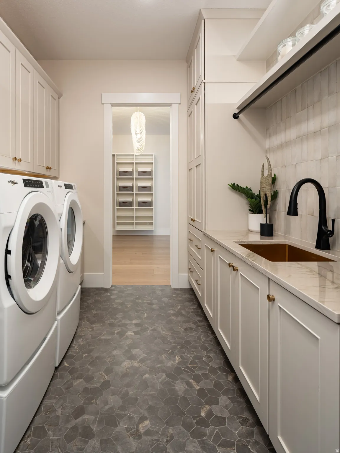 Laundry room featuring a dark polygonal tile floor, light-toned cabinetry with brass hardware, a copper-toned sink with a matte black faucet, and a light-toned countertop