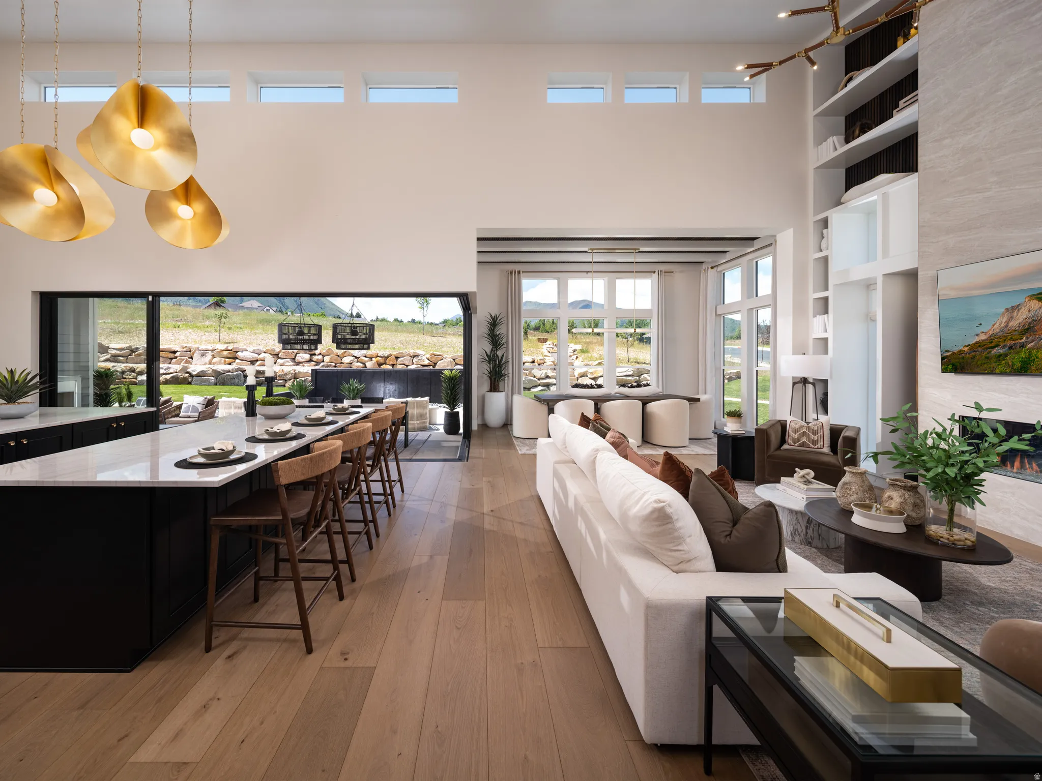 Open-concept living space featuring high ceilings, wood-finish flooring, a kitchen island with seating, a built-in fireplace, and expansive sliding glass doors