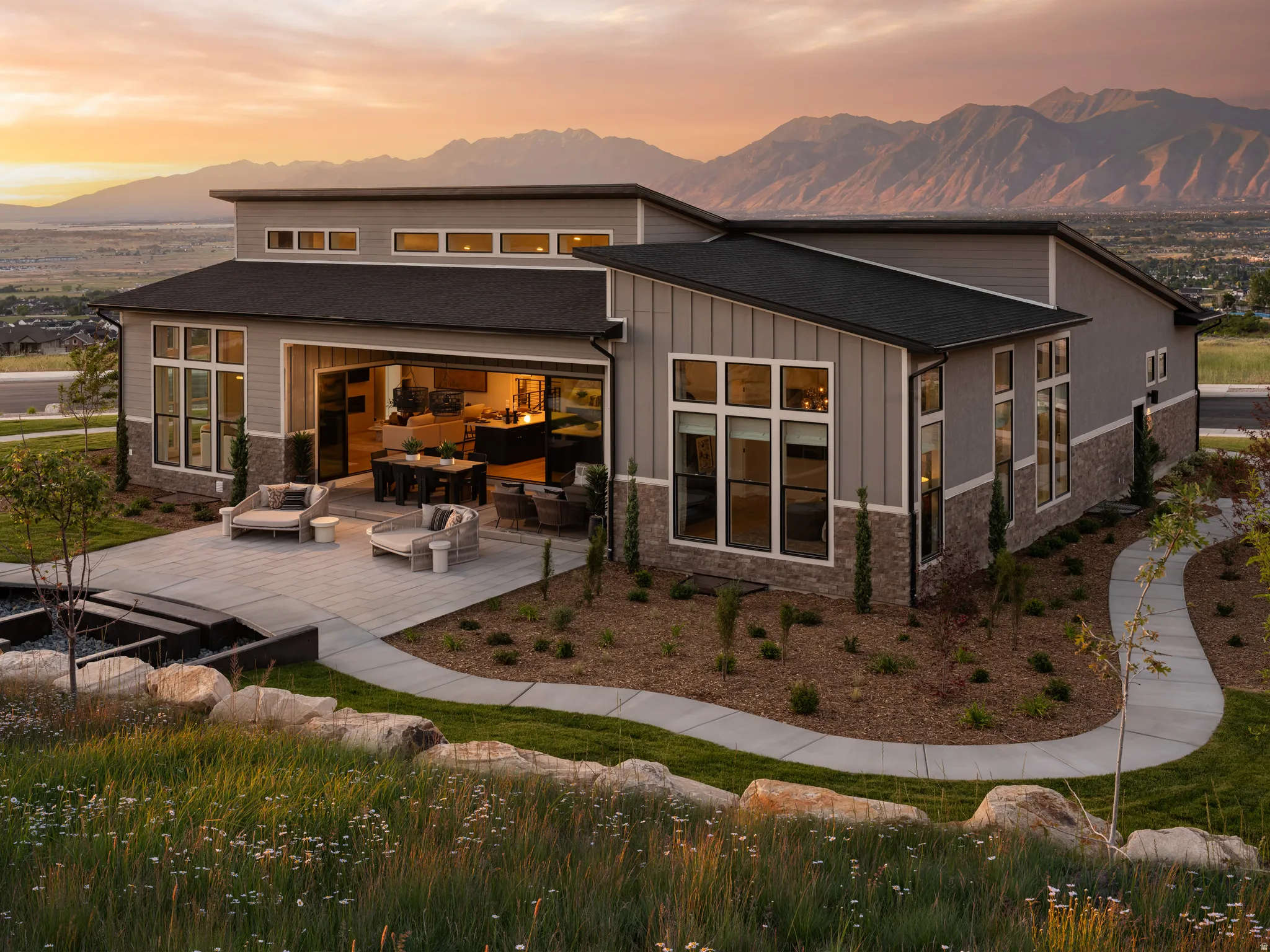 Modern exterior design featuring broad windows, a spacious patio, and a mountain backdrop