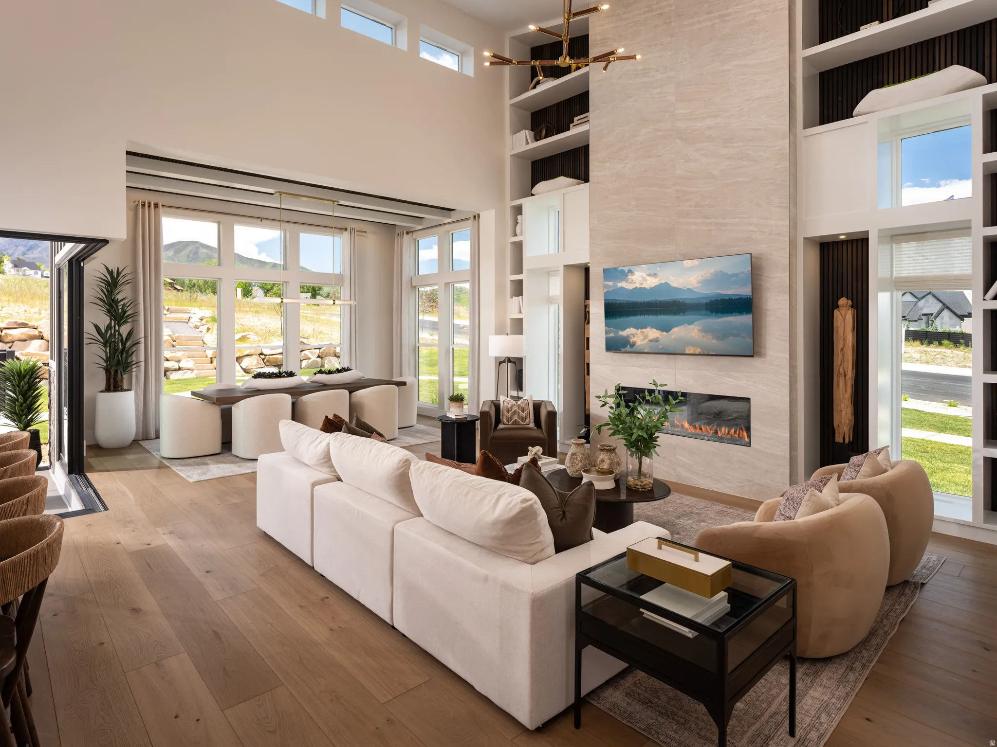 Expansive living area with a high ceiling, wood-finish flooring, a full-height fireplace with an integrated linear firebox, a large dining area, and multiple oversized windows