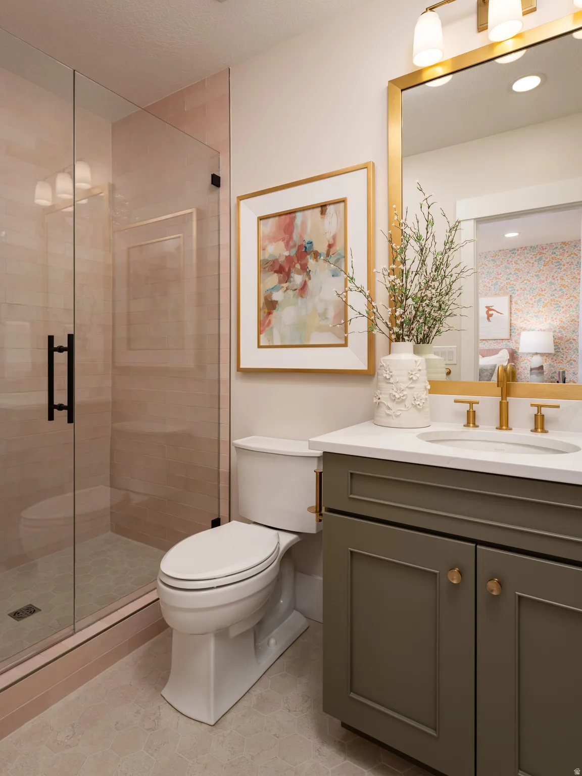 Bathroom featuring a glass-enclosed shower with tile surround, a single vanity with a white countertop and gold-toned fixtures, a framed mirror with integrated lighting, and hexagonal floor tiling
