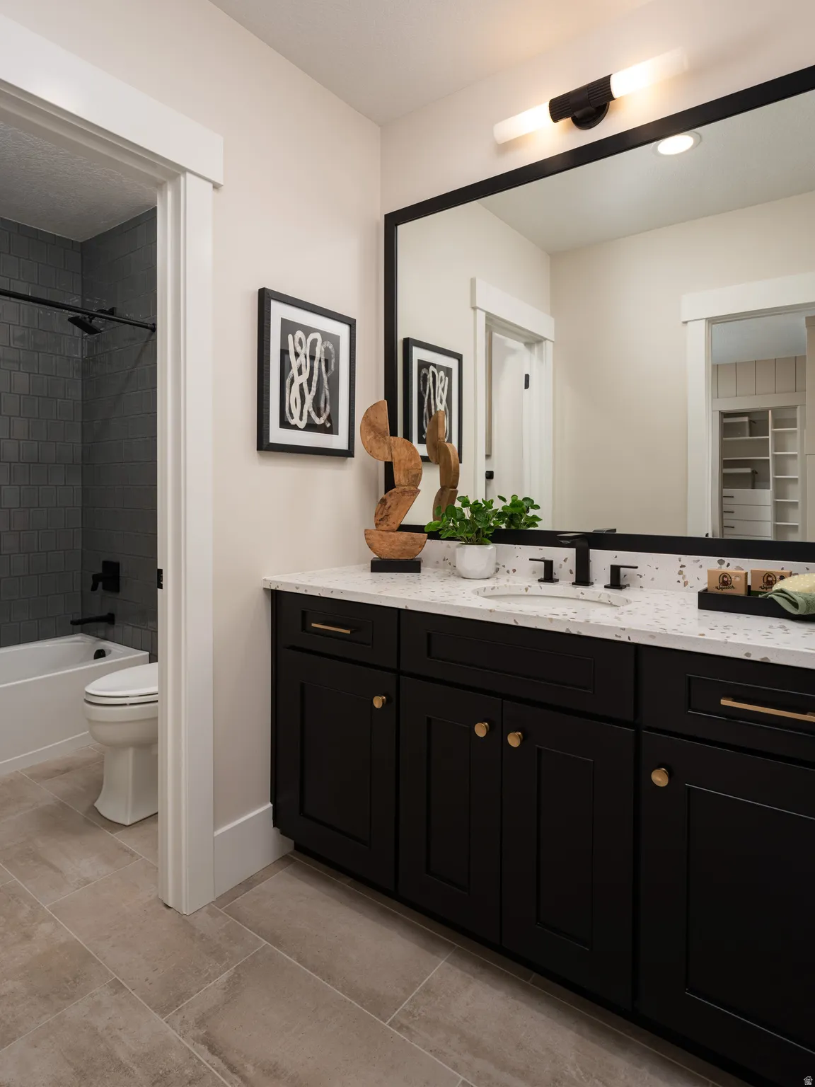 Bathroom vanity featuring black cabinetry with gold-finish hardware, a speckled countertop, and an integrated sink with a matte black faucet