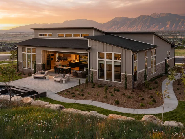 Modern exterior design featuring broad windows, a spacious patio, and a mountain backdrop