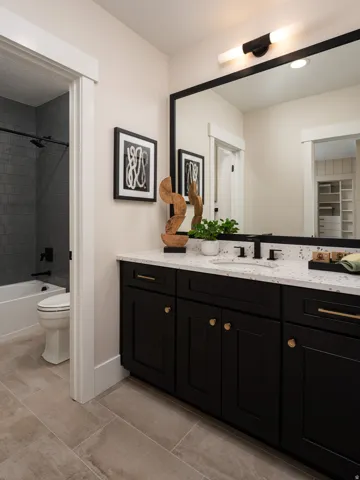 Bathroom vanity featuring black cabinetry with gold-finish hardware, a speckled countertop, and an integrated sink with a matte black faucet