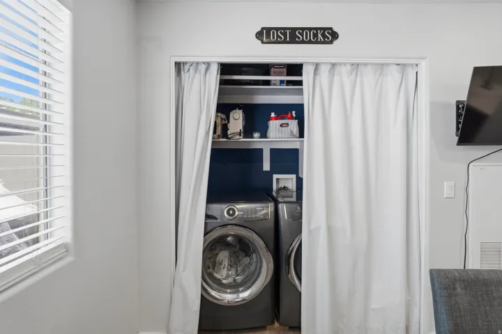 Dedicated laundry closet featuring a built-in shelf, deep blue accent wall, and space for a side-by-side washer and dryer