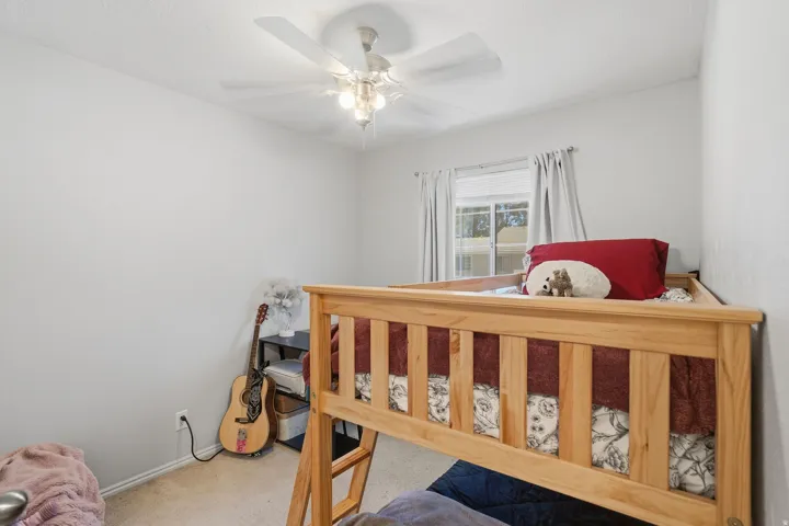 Room featuring light-colored walls, carpet flooring, a ceiling fan with integrated lighting, and a window with curtains
