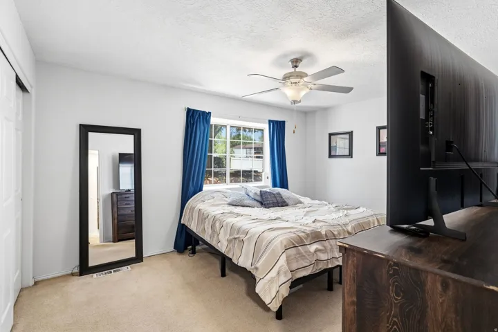 Bright bedroom featuring a ceiling fan with integrated lighting, a large window with blue drapes, and a full-length mirror