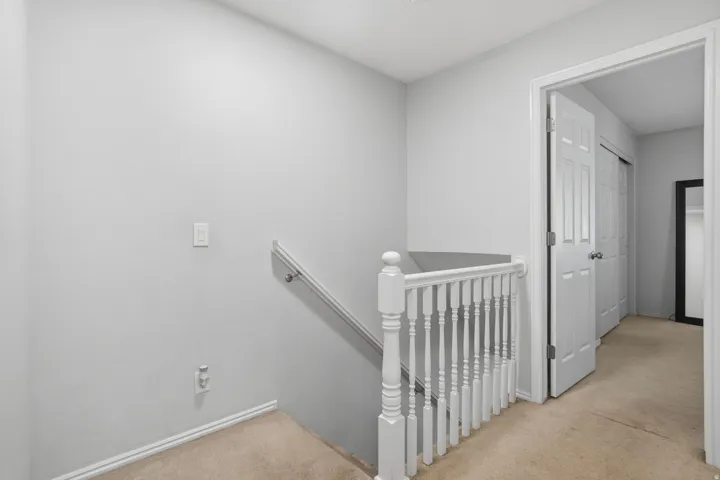 Carpeted hallway featuring a white baluster railing and a white paneled door