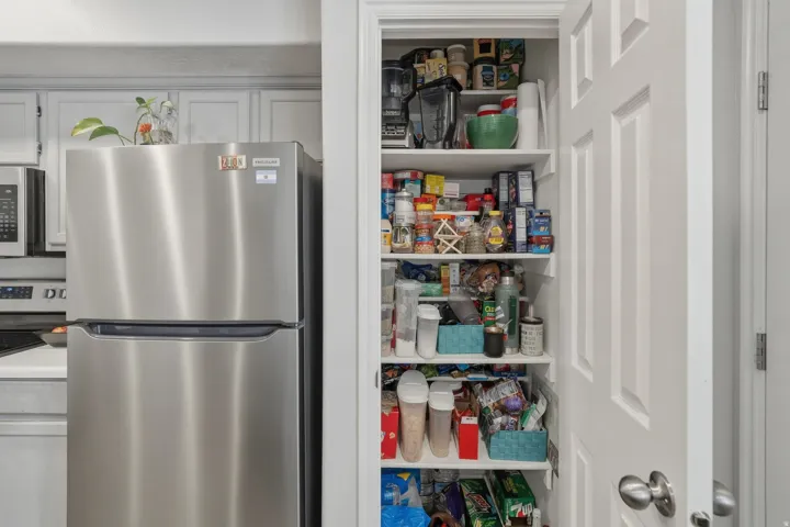 Built-in pantry with multiple white shelving units and a white paneled door, offering extensive storage capacity