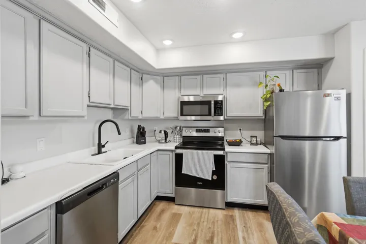 Modern kitchen featuring light gray cabinetry, stainless steel appliances, wood-finish flooring, white countertops, and recessed lighting