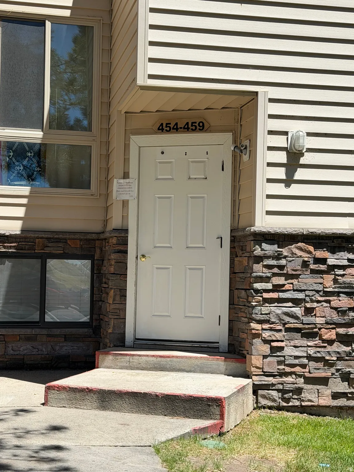 Entryway featuring a white paneled door with brass hardware, stacked stone veneer, light beige horizontal siding, and concrete steps