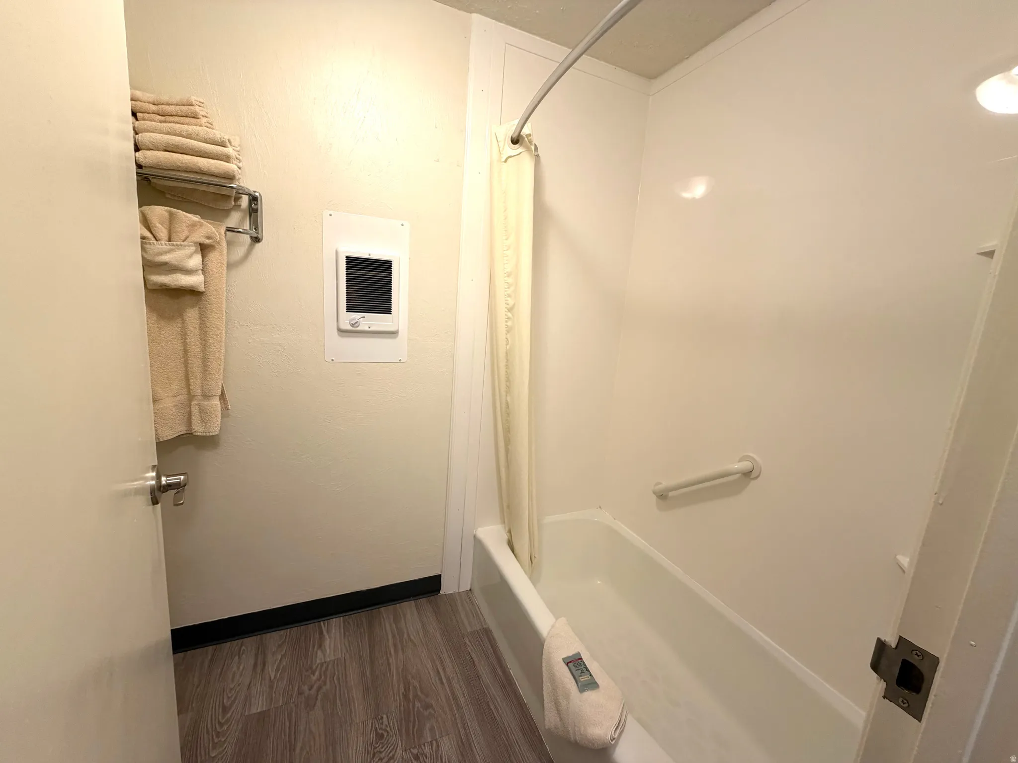 Bathroom featuring a white tub, shower curtain rod, and light wood-finish flooring