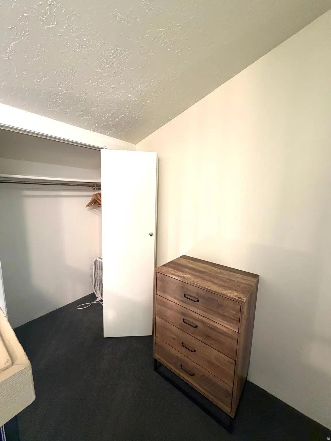 Built-in closet with hanging rod, featuring a white bi-fold door and dark carpeting