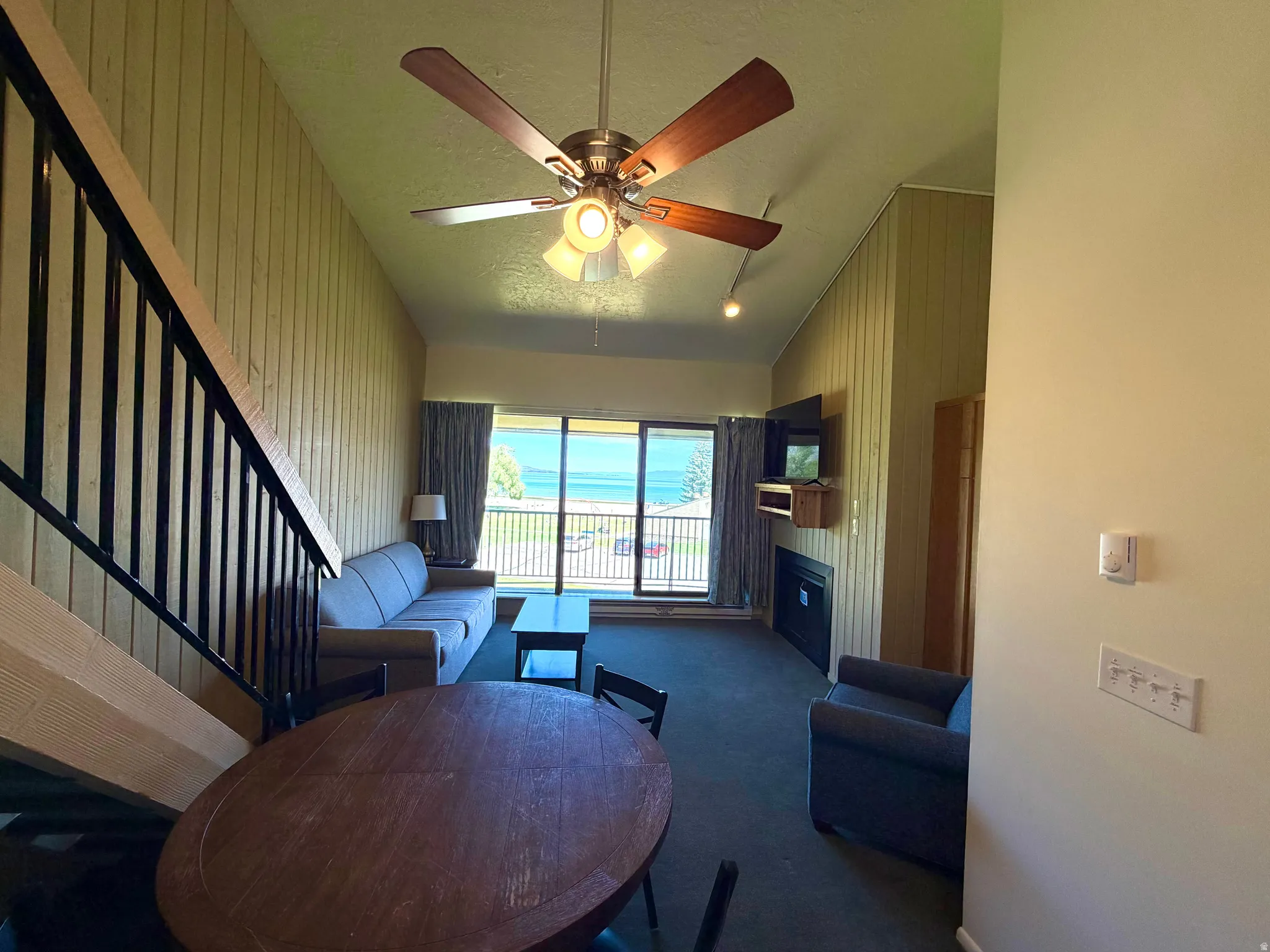 Living area featuring a ceiling fan with light fixture, vertical paneling accent wall, and a fireplace with a mantel shelf