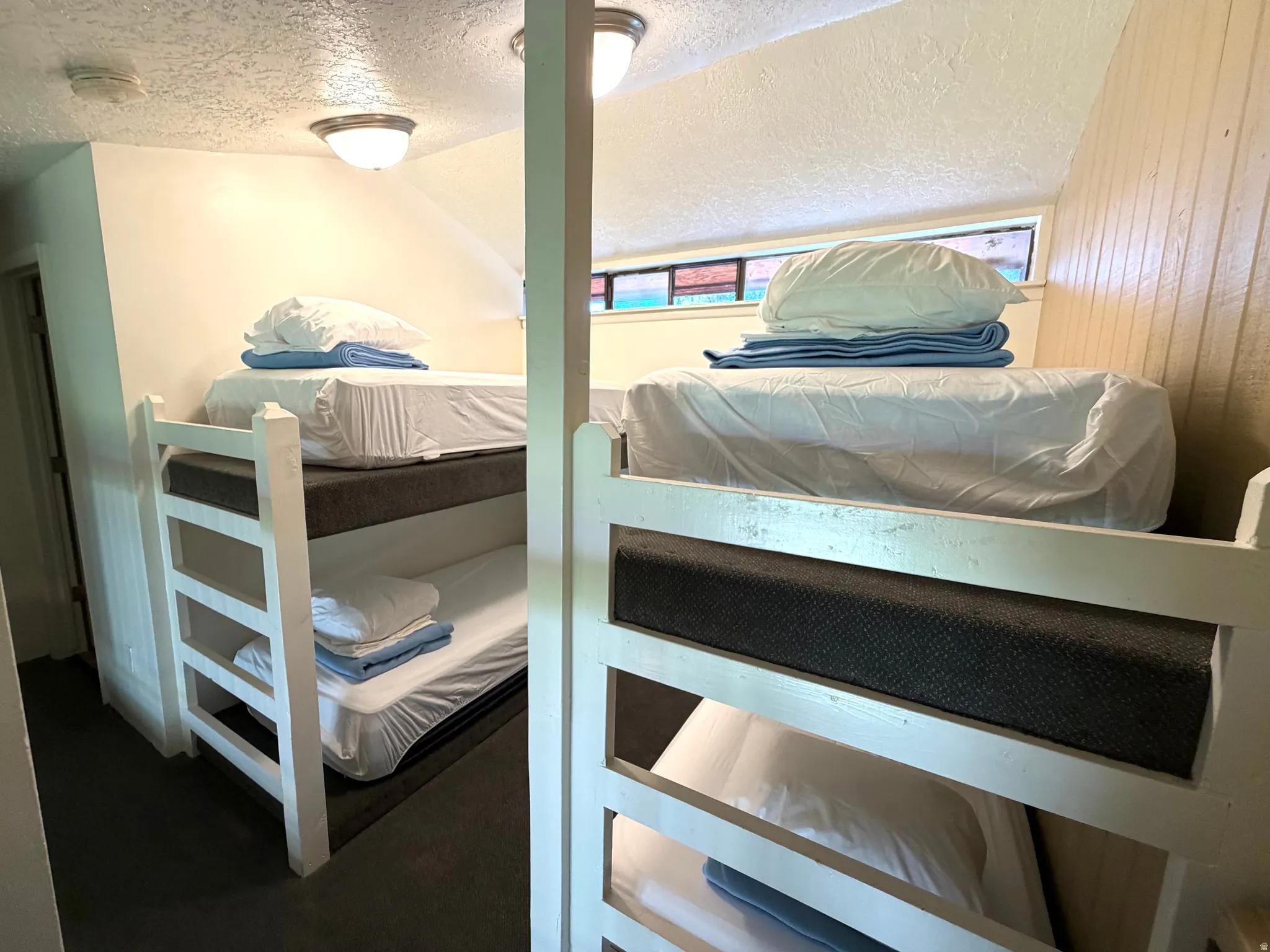 Built-in bunk beds with white frames, textured dark gray mattresses, and overhead flush-mount lighting fixtures