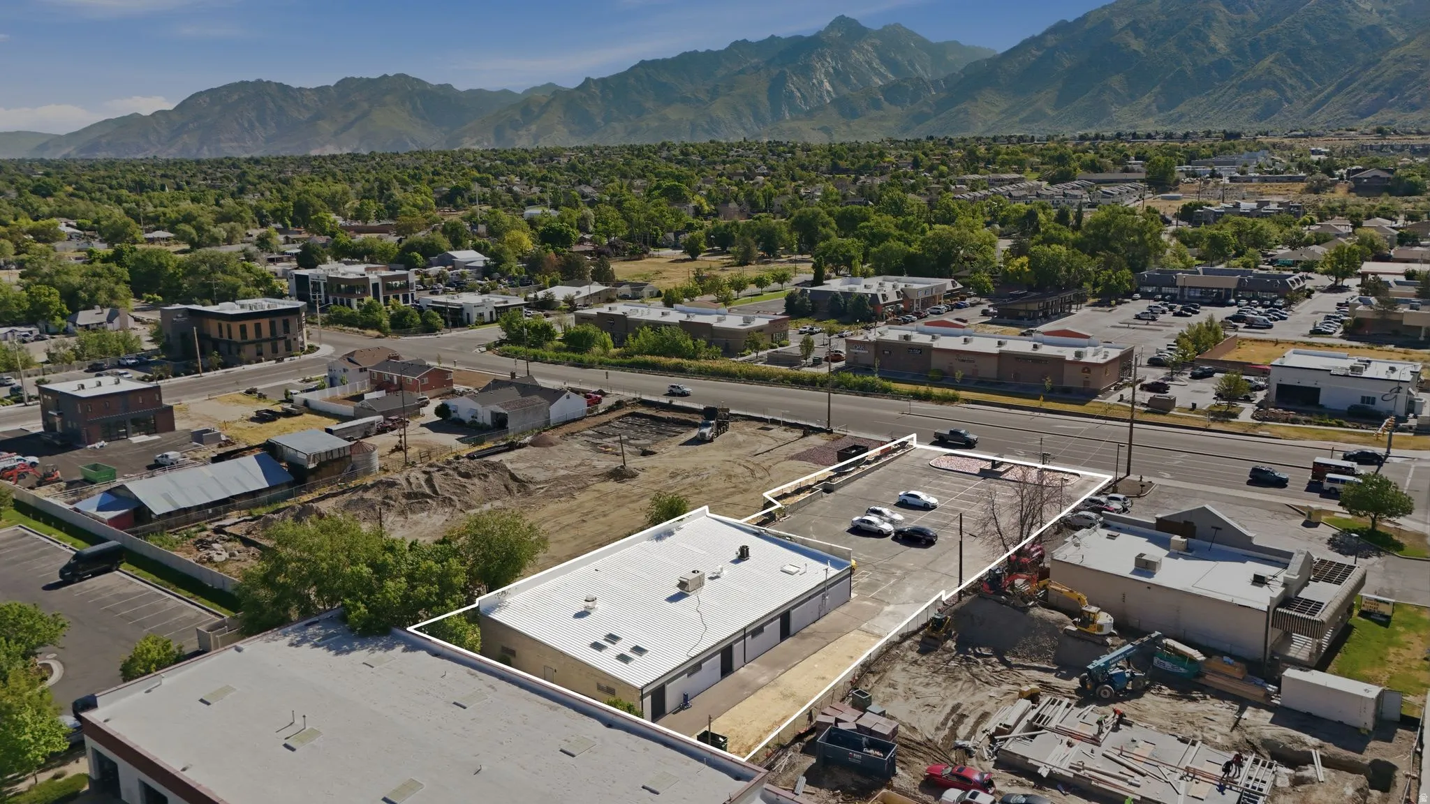 Commercial property featuring a flat roof structure with a paved parking area and an expansive undeveloped lot