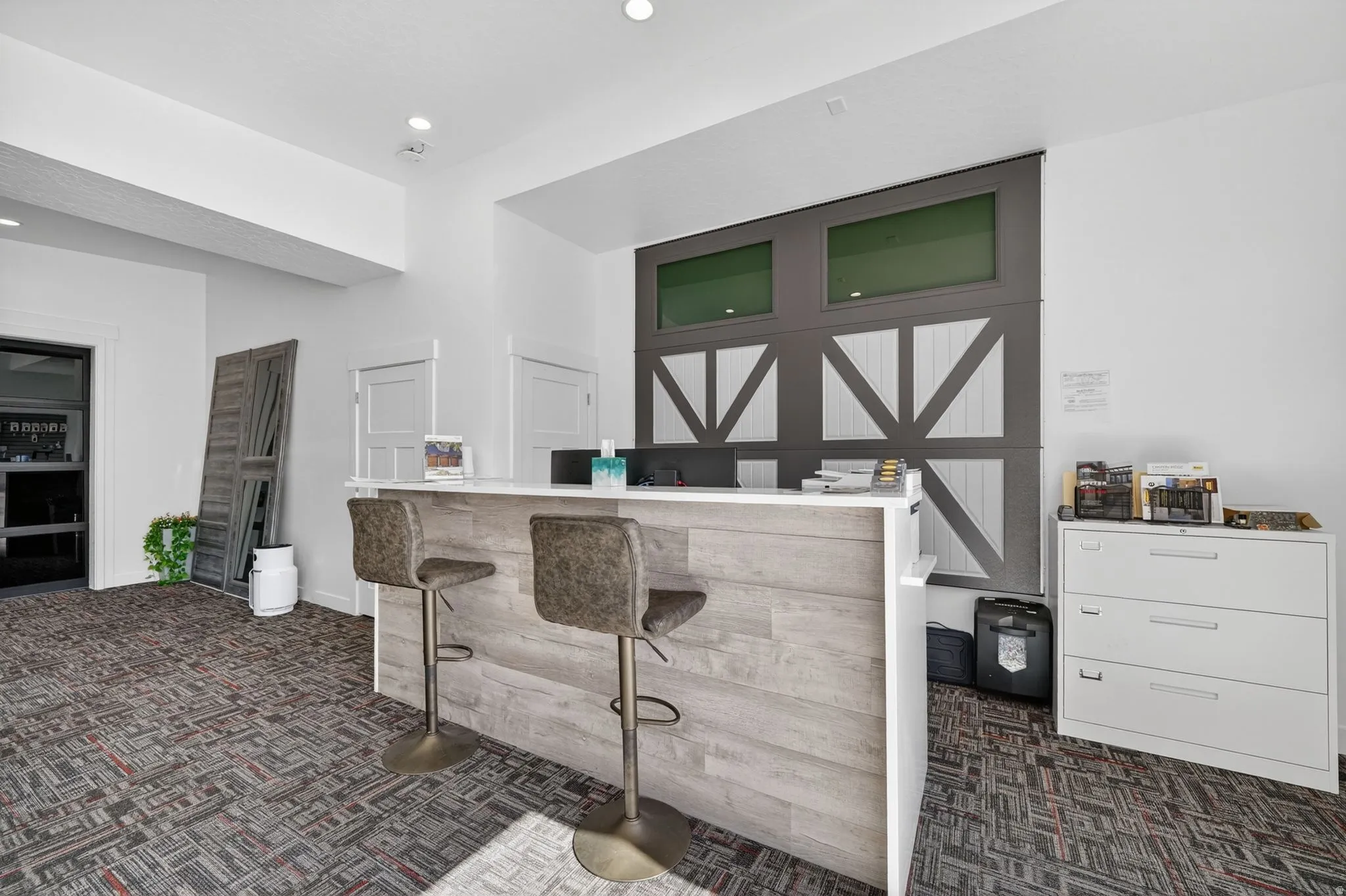 Modern reception area featuring a light wood-finish reception desk with white countertop, recessed lighting, and patterned carpet flooring