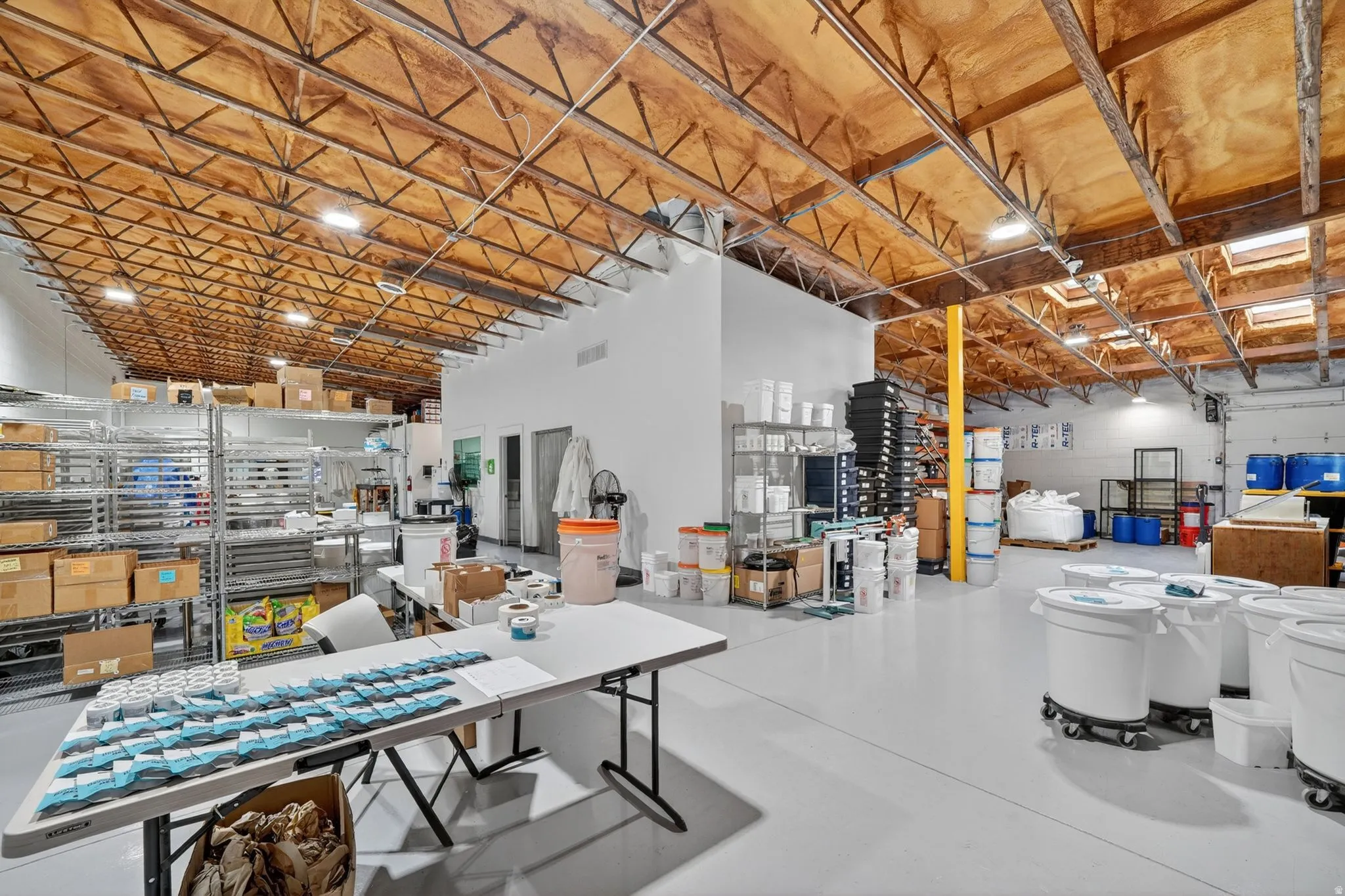 Expansive industrial space featuring a light-colored concrete floor and exposed wood-beam ceiling with metal trusswork