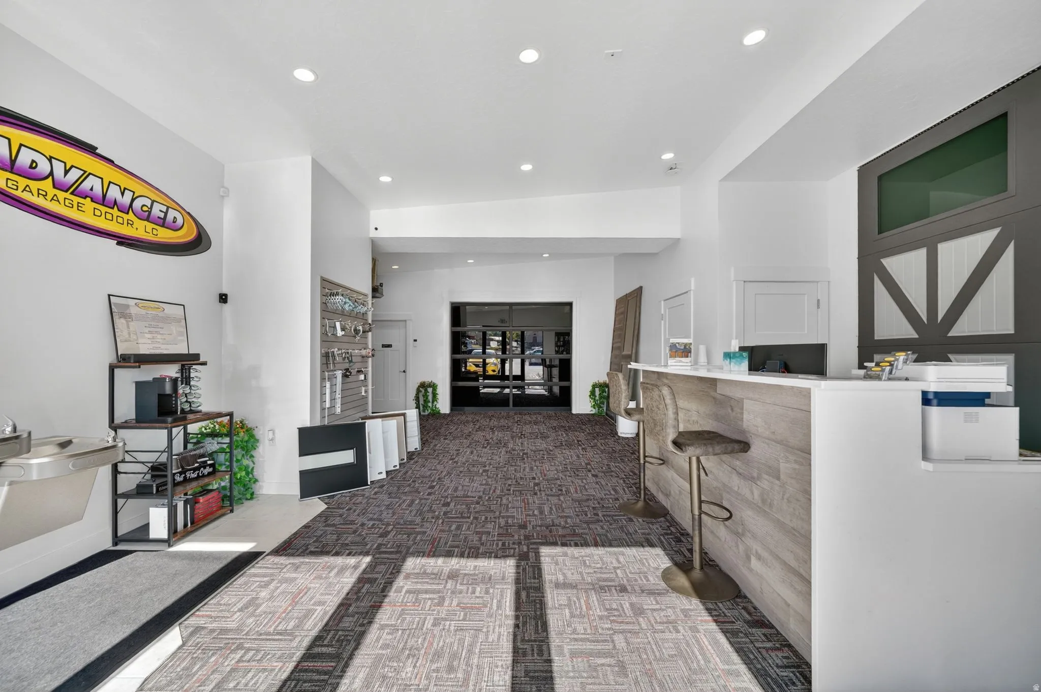 Spacious reception area featuring recessed lighting, patterned carpet flooring, a wood-finish reception desk with counter seating, and a decorative wall panel