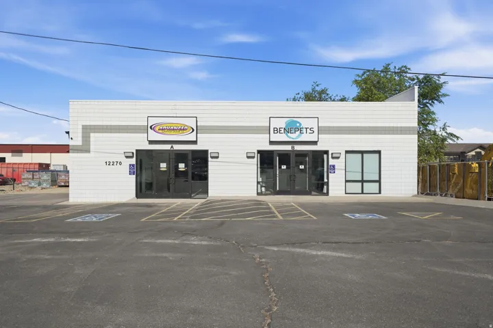 Commercial building with a textured white facade, multiple storefront entrances, and an asphalt parking lot with marked spaces
