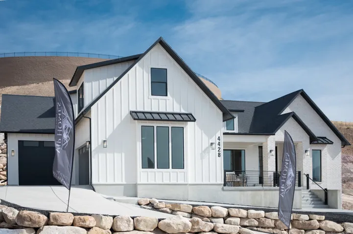 Modern farmhouse exterior featuring white board and batten siding, white brick, black-framed windows, a covered porch with dark railing, and a dark garage door