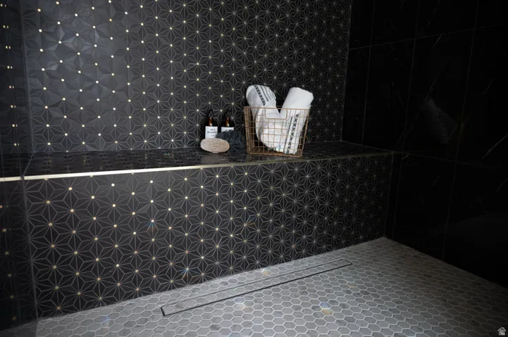 Shower featuring geometric patterned wall tile with gold accents, a dark stone bench, and large format black wall tile