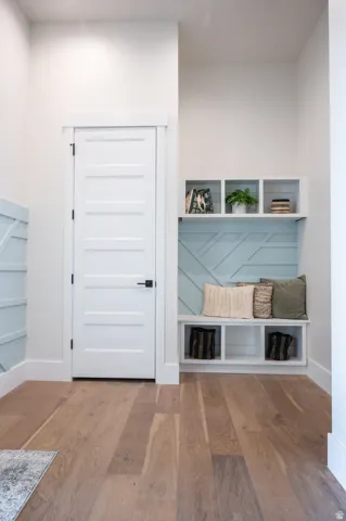 Entryway featuring wood-finish flooring, a white four-panel door with black hardware, and a built-in bench with cubby storage