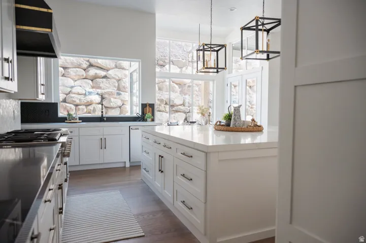 Kitchen featuring white shaker cabinetry, an expansive center island with a light-colored countertop, dark wood-finish flooring, and black geometric pendant lighting