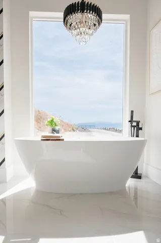 Freestanding soaking tub with a floor-mounted matte black faucet, set against a large picture window