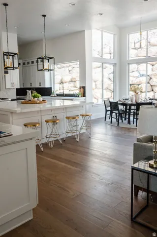 Spacious open-concept living area featuring wood-finish flooring, a kitchen island with a light-toned countertop, white cabinetry with dark hardware, and tall windows