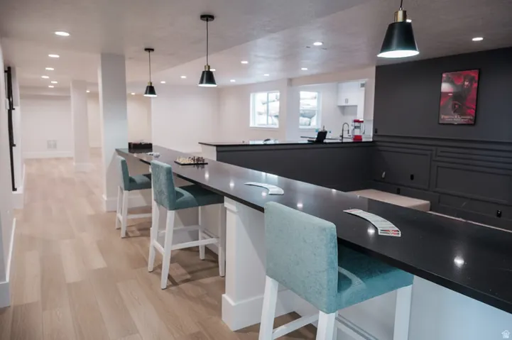 Spacious finished basement featuring wood-finish flooring, recessed lighting, and a long dark countertop bar area with pendant lighting