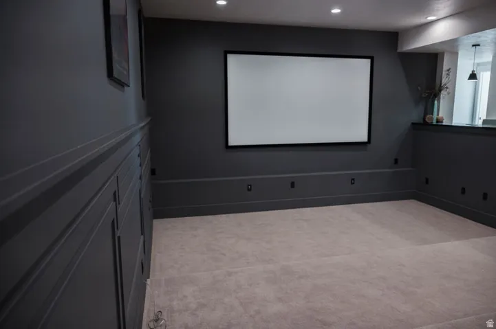 Dedicated media room featuring a large projection screen, dark paneled wainscoting, recessed lighting, and light-toned carpet flooring
