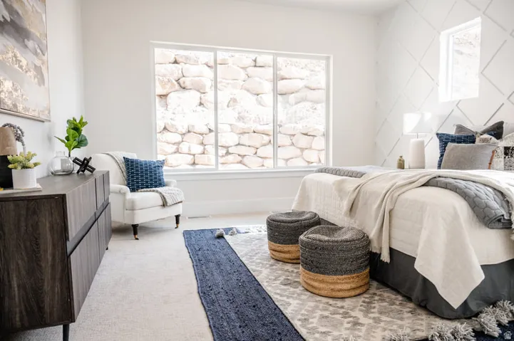 Spacious interior featuring a large multi-pane window, decorative accent wall, light-toned carpeting, and a dark wood-finish cabinet